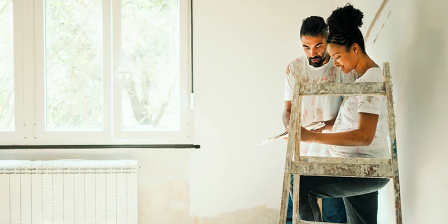 A young couple who saved money for a home improvement project with a Build-A-Buck account are on a ladder and painting
