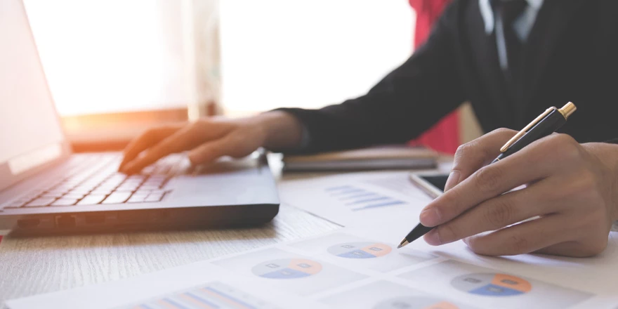 Close up of a business manager working with printed charts and on a laptop to implement accounts payable services