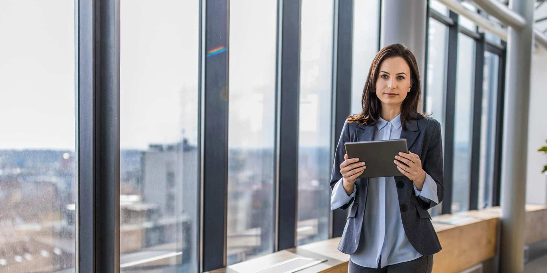 A businesswoman on a tablet utilizes foreign exchange in front of an office overlooking the city