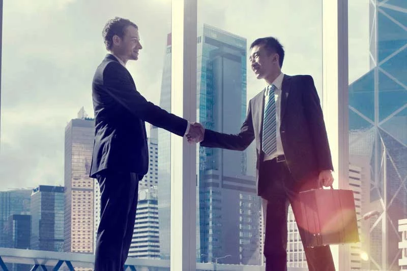 Two businessmen on an international services team shake hands in front a city window