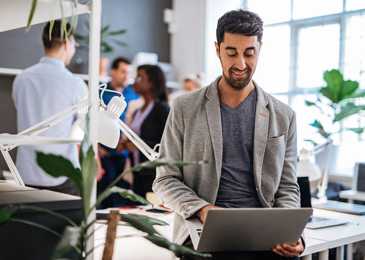 A businessman in a busy office is using his laptop to access Treasury Management and business online banking services